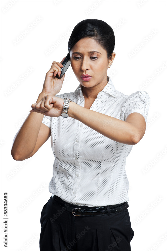 Businesswoman checking the time while talking on a mobile phone Businesswoman checking the time while talking on a mobile phone