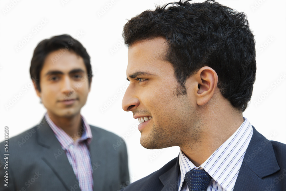 Close-up of a businessman smiling with his colleague in the background Close-up of a businessman smiling with his colleague in the background