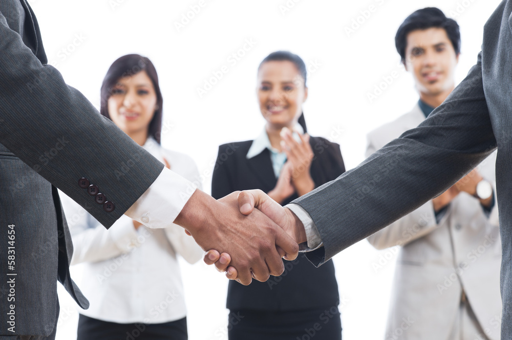Two businessmen shaking hands with their colleagues applauding Two businessmen shaking hands with their colleagues applauding