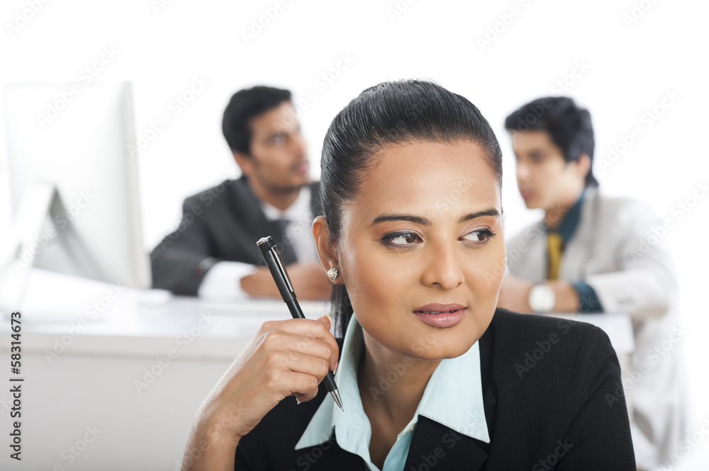 Close-up of a businesswoman holding a pen with her colleagues in the background Close-up of a businesswoman holding a pen with her colleagues in the background