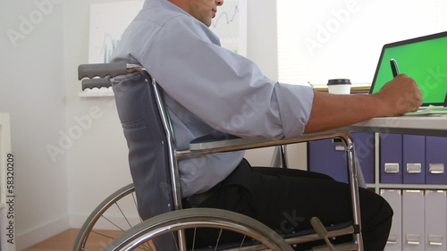 Hispanic business man in wheelchair using laptop with greenscree photo