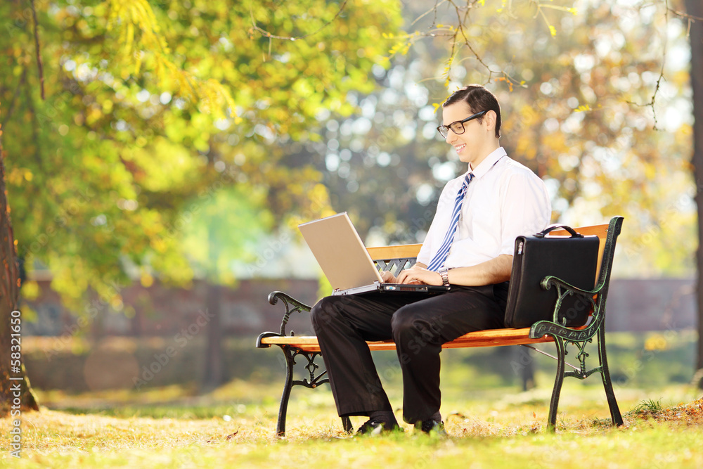 Smiling businessperson sitting on bench working on a laptop Smiling businessperson sitting on bench working on a laptop
