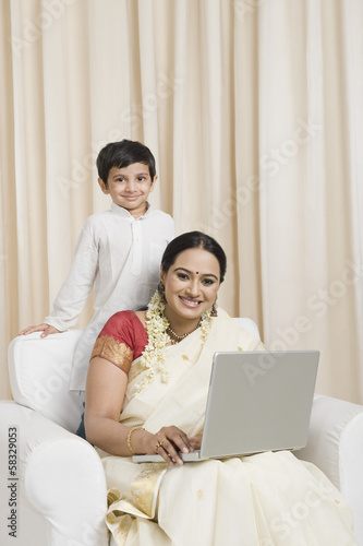 Woman using a laptop with her son standing behind her