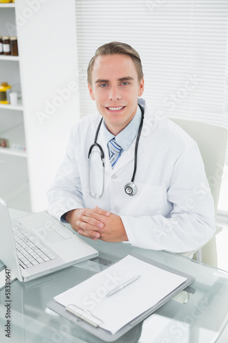 Smiling male doctor with laptop at medical office