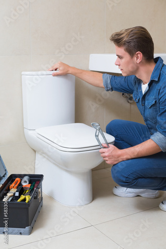 Handsome plumber with toolbox doing toilet reparation