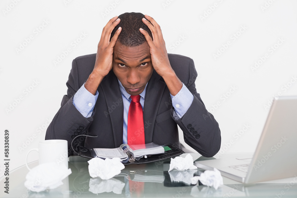Frustrated Afro businessman with head in hands at desk Frustrated Afro businessman with head in hands at desk