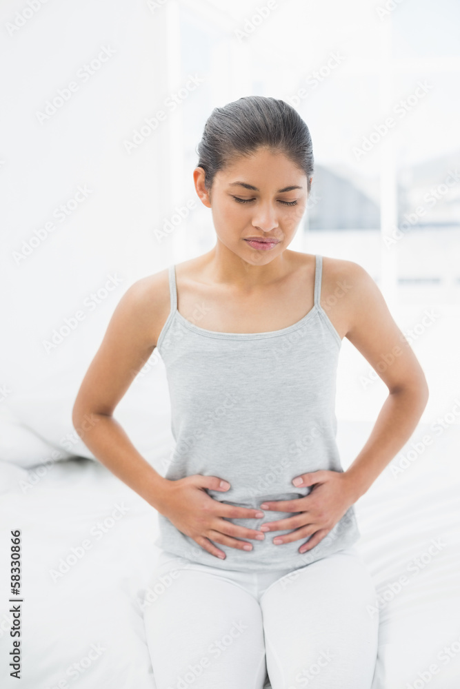Casual woman with stomach pain sitting in bed Casual woman with stomach pain sitting in bed