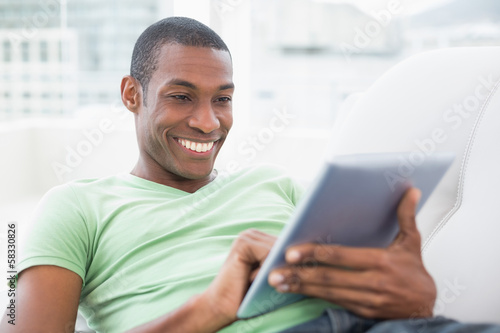 Casual smiling Afro man using digital tablet on sofa