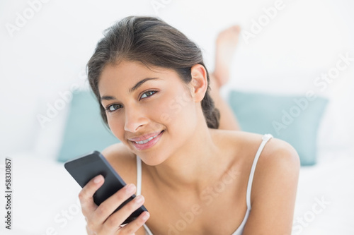 Smiling woman with mobile phone in bed
