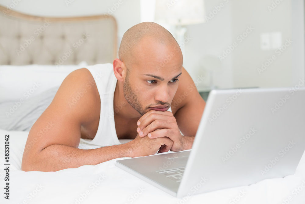 Serious casual bald man using laptop in bed Serious casual bald man using laptop in bed