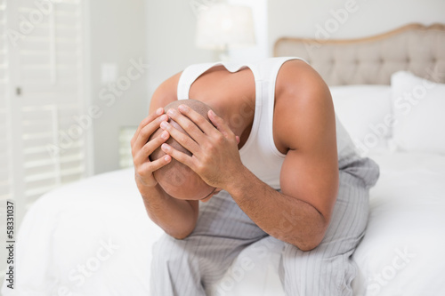 Thoughtful bald man with head in hands on bed