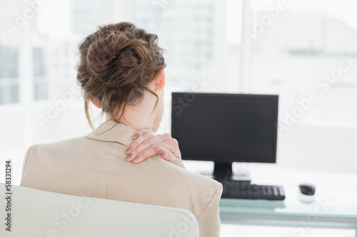 Rear view of businesswoman with neck pain in office photo