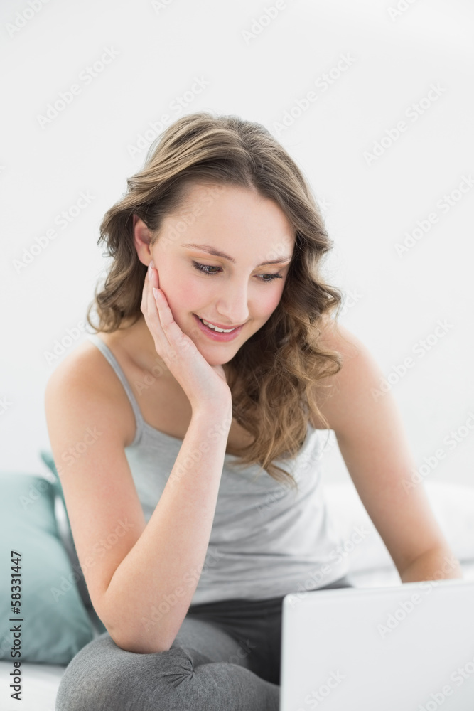 Smiling casual brunette looking at laptop in bed Smiling casual brunette looking at laptop in bed