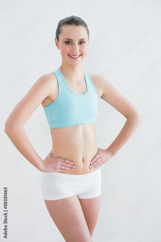 Obraz premium Smiling toned woman with hands on hips against wall