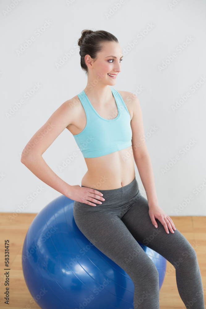 Fototapeta premium Smiling fit woman on exercise ball in fitness studio