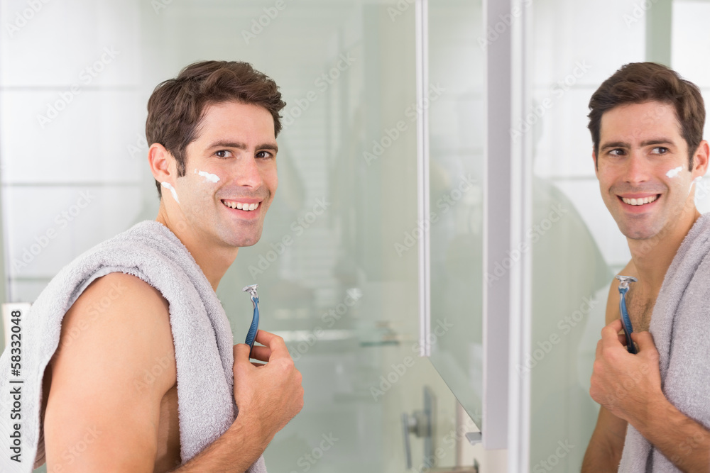 Smiling handsome man with reflection shaving in bathroom