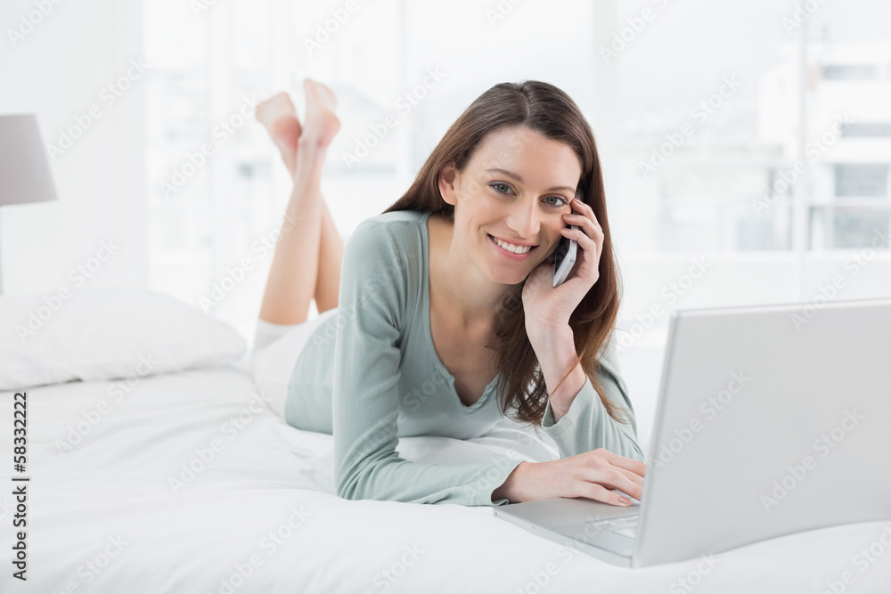 Smiling casual woman using cellphone and laptop in bed Smiling casual woman using cellphone and laptop in bed