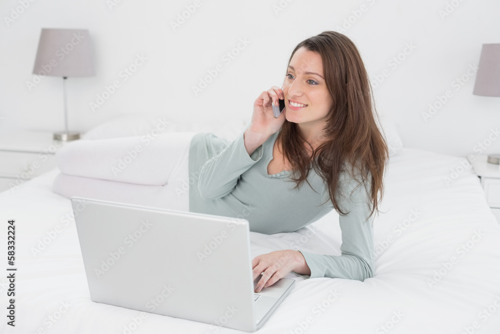 Smiling casual woman using cellphone and laptop in bed Smiling casual woman using cellphone and laptop in bed