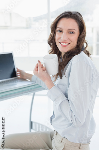 Businesswoman with coffee cup in front of laptop in office
