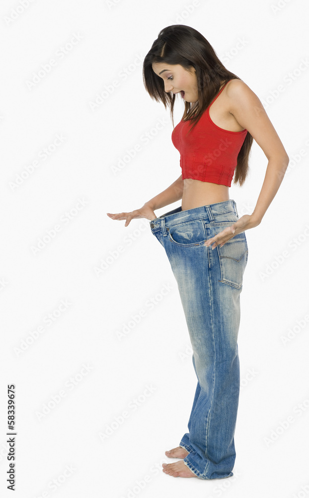 Woman pulling jeans from waistline to show weight loss and looking shocked Woman pulling jeans from waistline to show weight loss and looking shocked