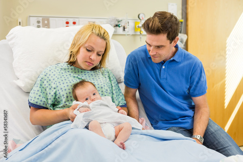 Couple Looking At Newborn Baby In Hospital Room © Tyler Olson