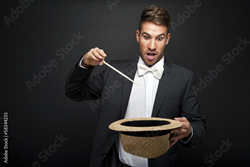 Obraz na płótnie A magician in a black suit holding an empty top hat and magic wa