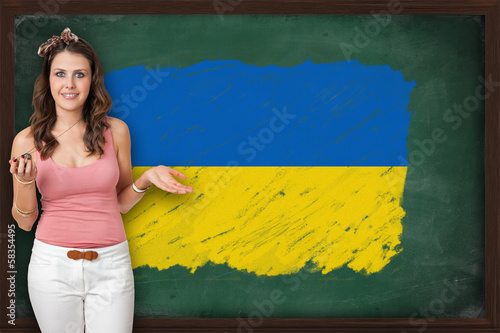 Beautiful and smiling woman showing flag of Ukraine on blackboar