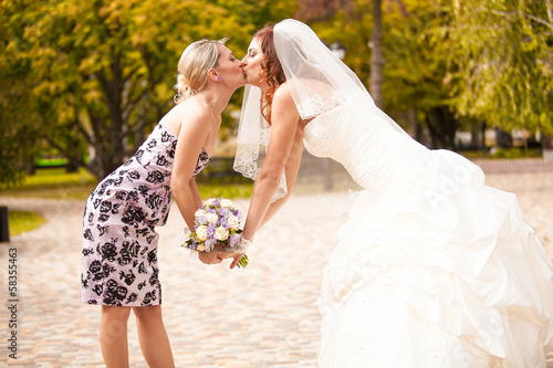 Valokuvatapetti Outdoor portrait of bridesmaid kissing beautiful bride