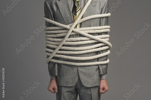 Mid section view of a businessman tied up with ropes