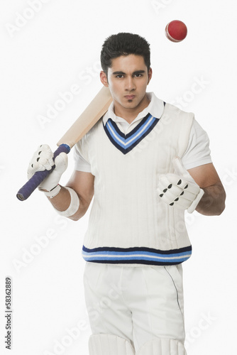 Obraz na płótnie Cricket batsman holding a bat and tossing a ball