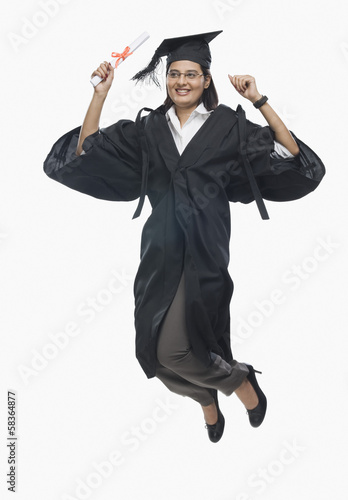 Woman jumping with her diploma in graduation gown 