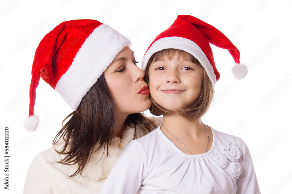 Happy mother kissing daughter on cheek in Christmas hat Happy mother kissing daughter on cheek in Christmas hat