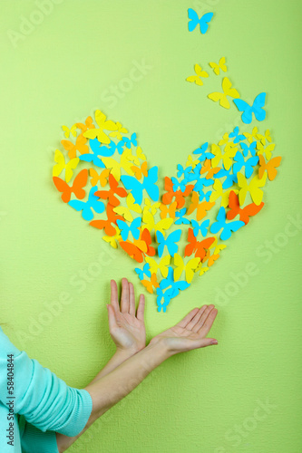 Paper butterflies on hands on green wall background