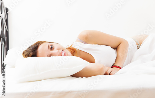Cheerful red-haired girl lying on white sheet