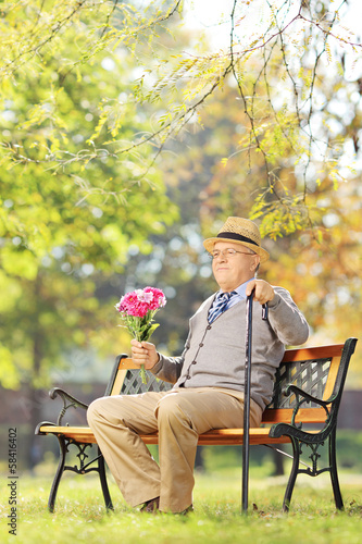 Senior gentleman with bouquet of flowers sitting on a bench, in