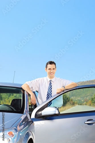 Smiling guy posing next to his car on an open road © Ljupco Smokovski
