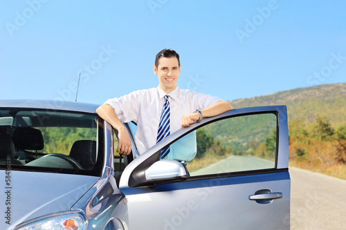 Smiling young male with tie posing next to his car
