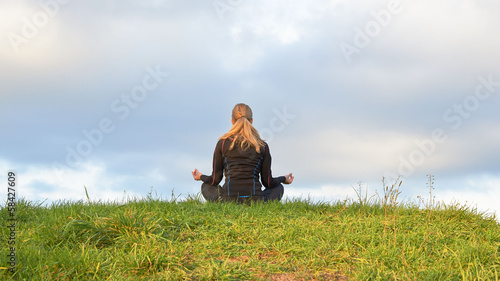 Pretty female doing yoga on top of the hill