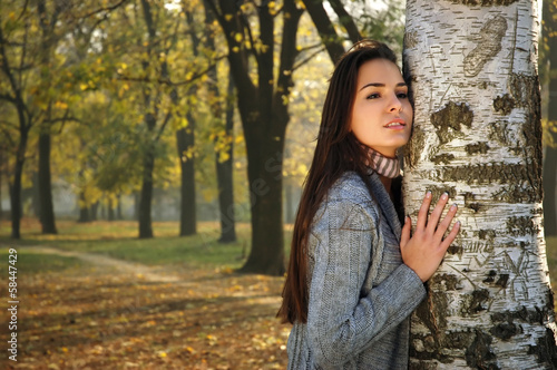 young pensive woman leaned on birch in autumn park