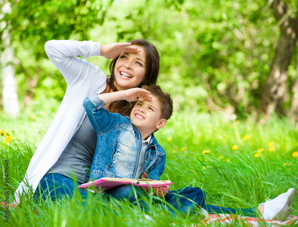 Mother and son with book sitting on green grass Mother and son with book sitting on green grass