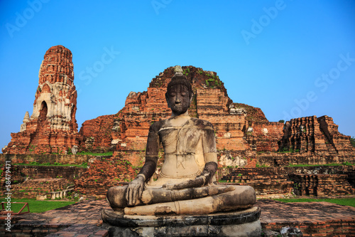 ancient big Buddha statue in front of damaged brick pagoda on bl