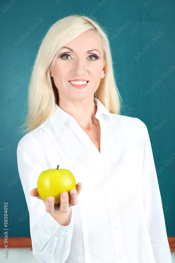 School teacher near blackboard with apple in classroom School teacher near blackboard with apple in classroom