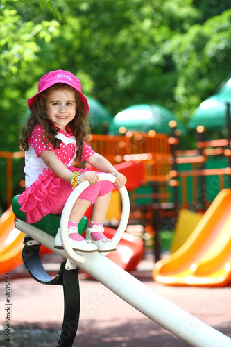 Portrait of a smiling little girl in a pink hat sitting on swing