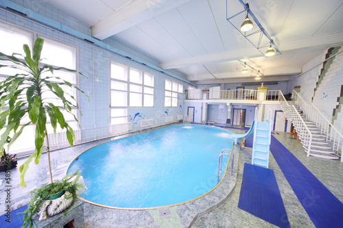 Empty oval indoor swimming pool with a small slide