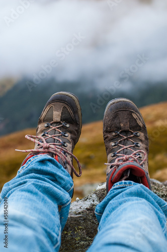 Dirty hiking shoes with mountains and clouds in the background © drimafilm