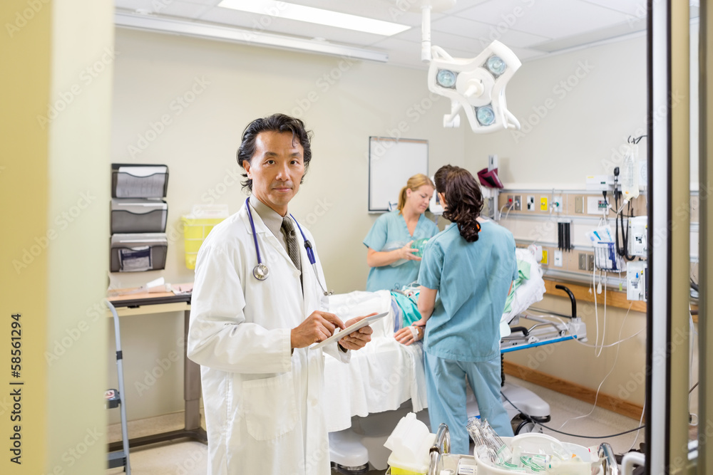 Doctor Holding Digital Tablet With Nurses Examining Patient Doctor Holding Digital Tablet With Nurses Examining Patient