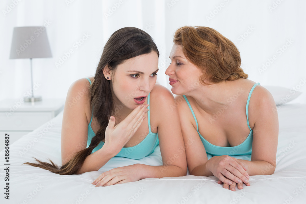 Female friends in tank tops gossiping in bed Female friends in tank tops gossiping in bed