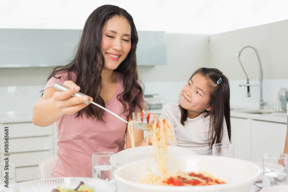 Girl watching happy woman serve spaghetti in kitchen Girl watching happy woman serve spaghetti in kitchen