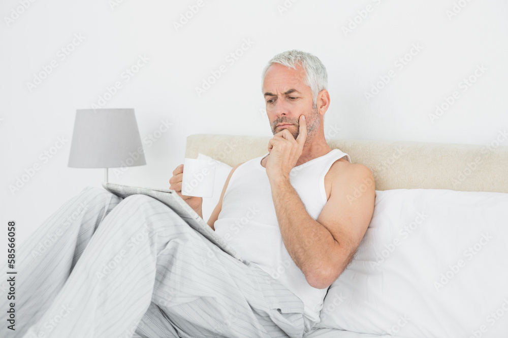 Man with coffee cup reading newspaper in bed Man with coffee cup reading newspaper in bed