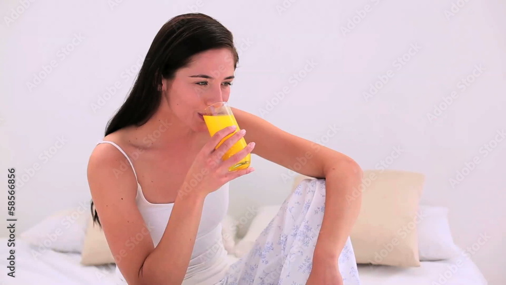Attractive brunette drinking a glass of orange juice in bed Attractive brunette drinking a glass of orange juice in bed